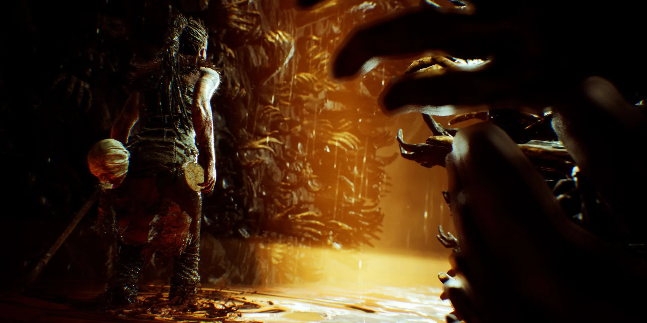 Senua đứng trước bức tường bàn tay trong game Hellblade Senua's Sacrifice